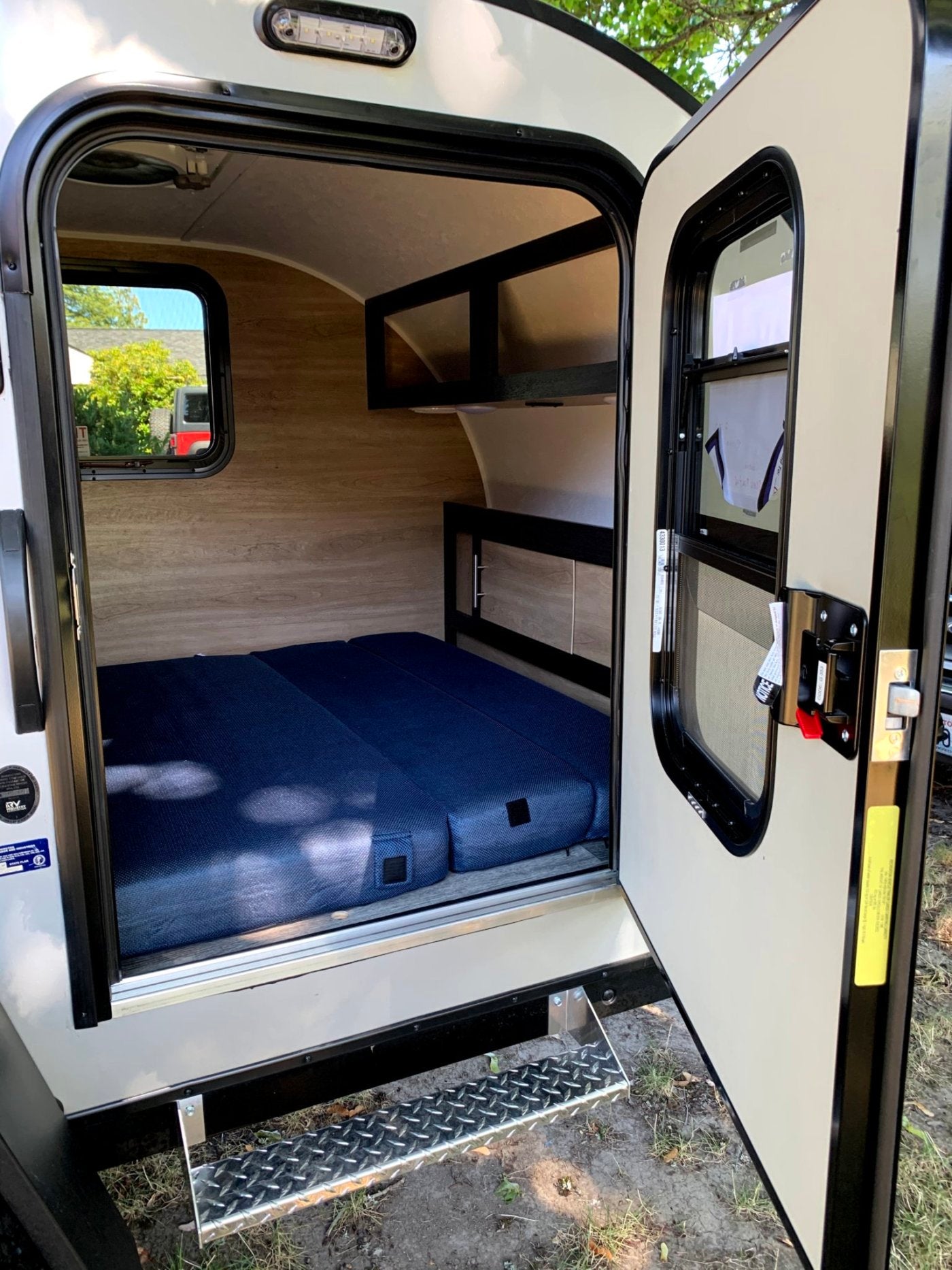 Step into this cozy RV rental! Features a compact interior with a comfy blue mattress, built-in shelving, and a window.