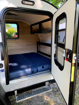 Step into this cozy RV rental! Features a compact interior with a comfy blue mattress, built-in shelving, and a window.