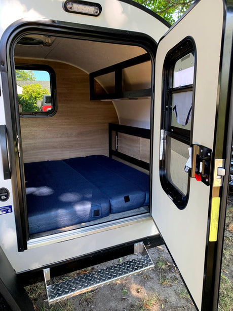 Step into this cozy RV rental! Features a compact interior with a comfy blue mattress, built-in shelving, and a window.