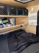 Cozy RV rental interior with organized storage shelves, crates, and a comfortable bed setup for your adventure.