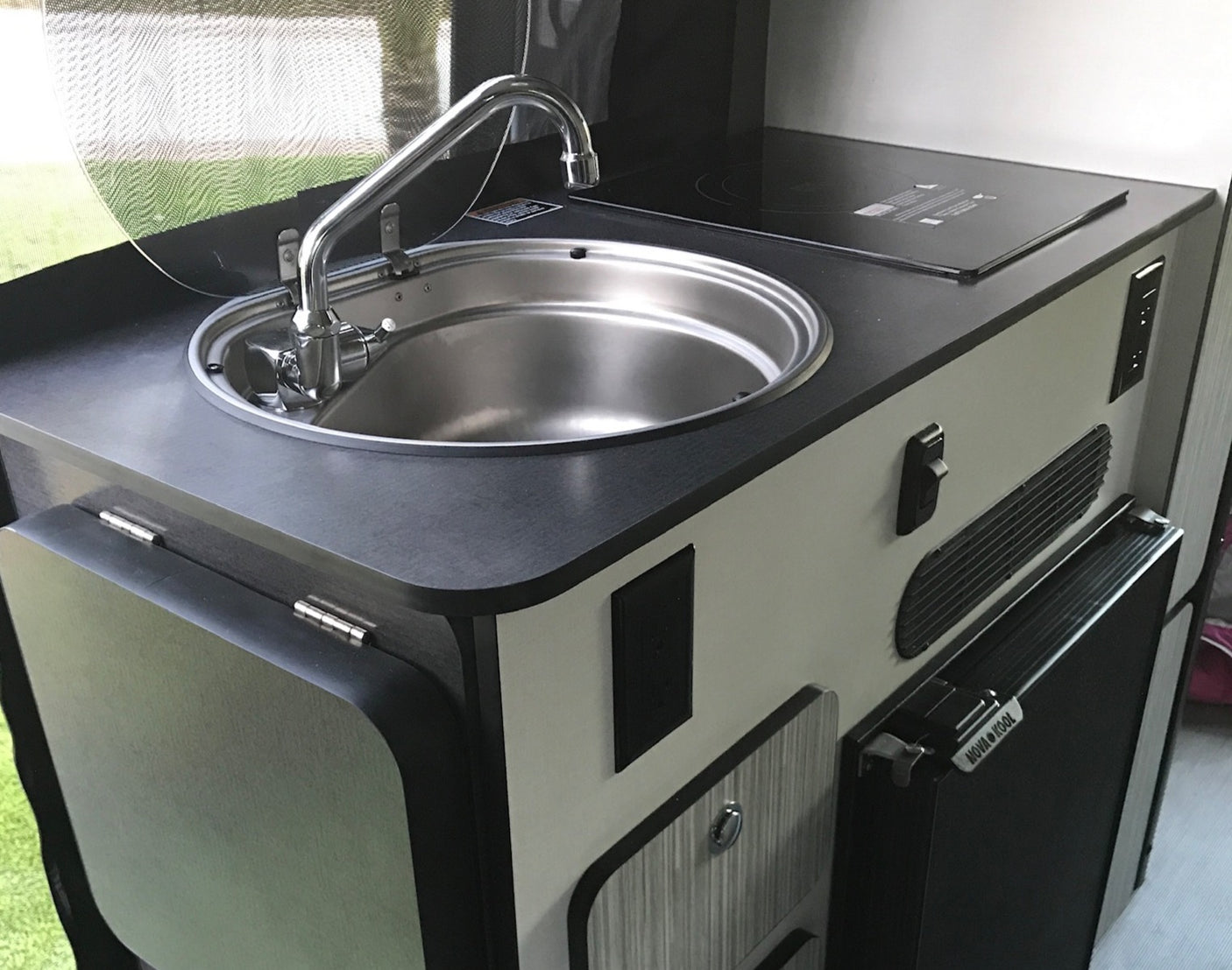 This RV rental features a compact kitchenette with a stainless steel sink, induction cooktop, and small refrigerator.