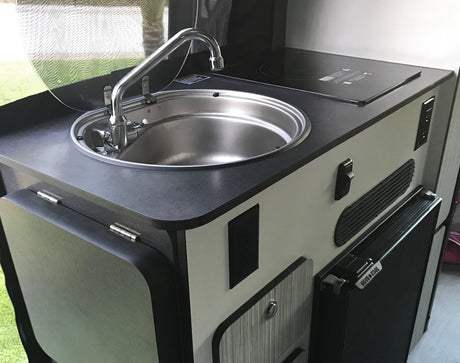 This RV rental features a compact kitchenette with a stainless steel sink, induction cooktop, and small refrigerator.