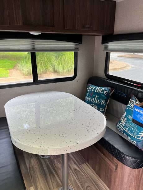 Inviting RV rental dinette with a speckled white table, black bench seating, and windows showing green outdoors.