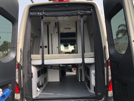 Inside a modern RV rental camper van: rear doors open to reveal an elevated bed and spacious storage.