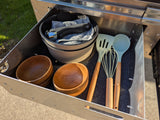 Organized RV rental drawer: collapsible pot, wooden bowls, and light-colored camping kitchen utensils.