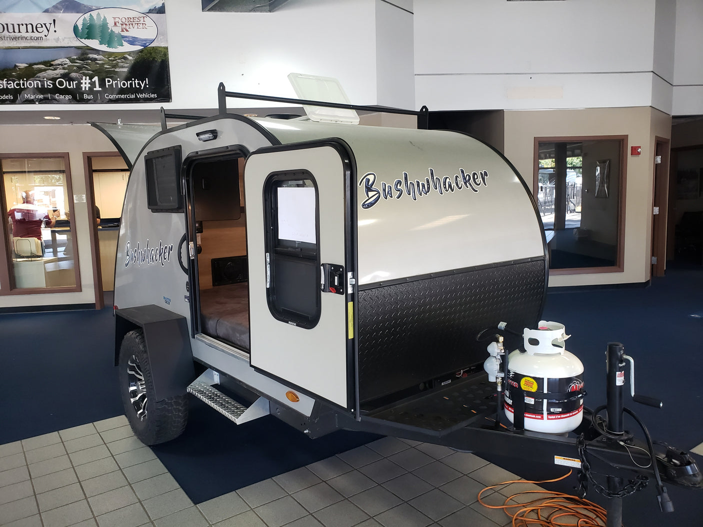 This Bushwhacker teardrop travel trailer, ideal for an RV rental, shows its compact design, cozy interior, and propane tank.