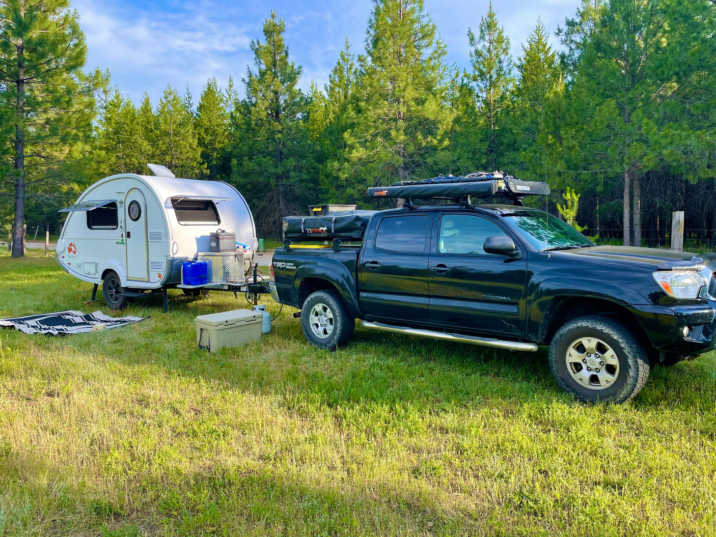 Black truck hitched to a white teardrop RV in a pine forest campsite. Your next RV rental adventure awaits!