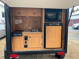 Compact outdoor kitchen of an RV rental: complete with sink, stove, microwave, and fridge, perfect for camping.