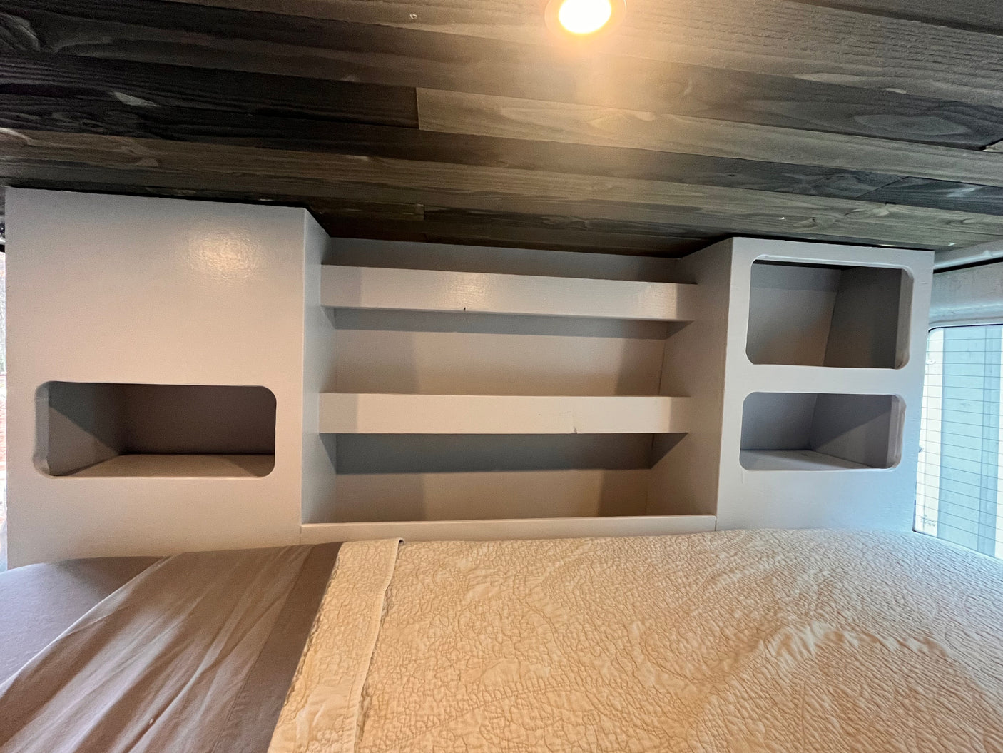 Cozy RV rental bedroom with built-in light grey storage cabinets, open shelves, and a comfortable bed under a wooden ceiling.