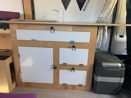 RV rental's compact camper van kitchen: sink, white cabinets, and an ICECO portable fridge for efficient storage.