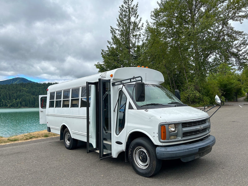 White bus-style rv rental parked at a scenic lake, nestled by mountains and forests, ideal for outdoor trips. — photo 2