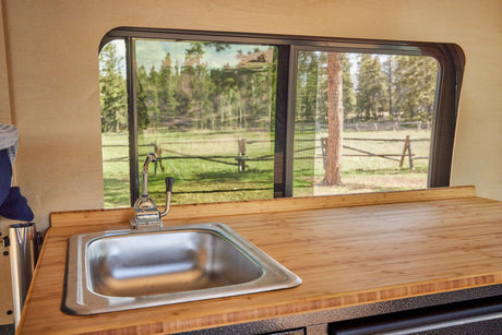 This RV rental boasts a functional kitchenette with a sink, bamboo counter, and a window framing a serene outdoor view.
