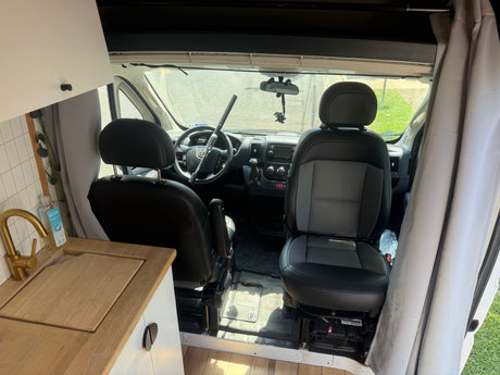 RV rental van interior: kitchenette with gold faucet, sink, and front cabin view with steering wheel and security bar.