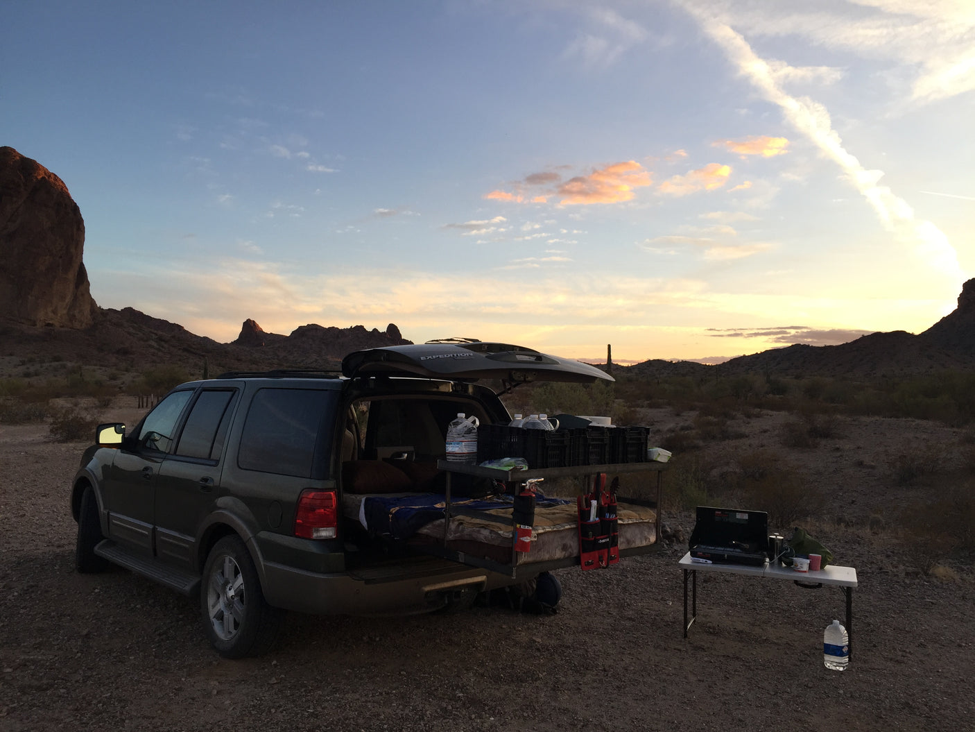 Desert sunset car camping in an SUV with a customized bed and kitchen. A practical RV rental alternative for adventure.