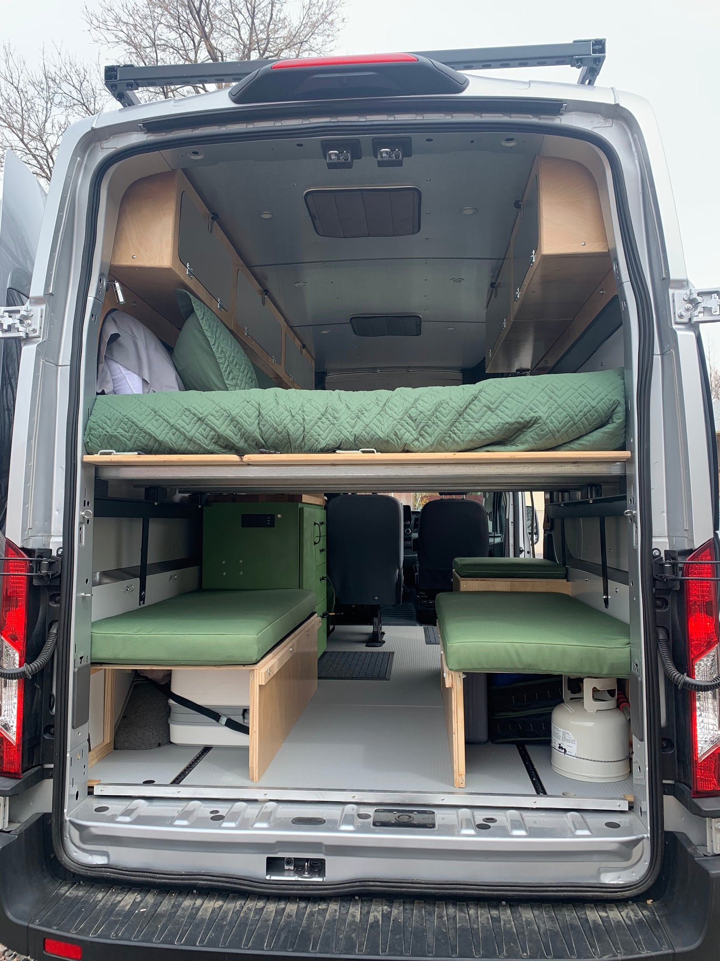 Spacious RV rental camper van interior with custom wooden storage, a cozy bed, and green cushioned seating.