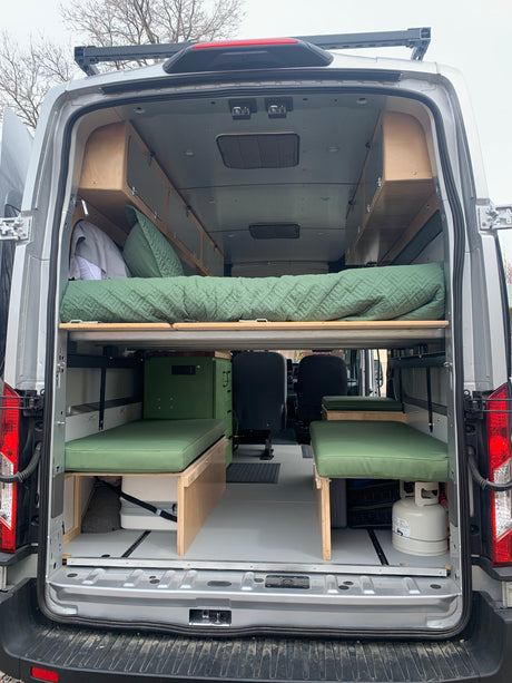 Spacious RV rental camper van interior with custom wooden storage, a cozy bed, and green cushioned seating.