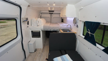 This rv rental camper van features a cozy interior with a rear bed, compact kitchen, and front seating.