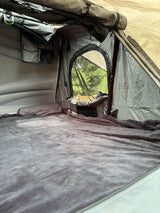 Inside a cozy roof-top tent: grey sleeping area, window view of trees, & storage. Ideal for an RV rental camping adventure.