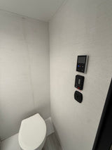 Compact RV rental bathroom with a white toilet and wall-mounted control panels, showcasing the efficient use of space.