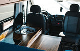 RV rental interior showcasing a modern kitchen with sink & stove, plus the front cabin area with driver & passenger seats.