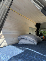 Bright RV rental interior: wood-paneled walls, warm LED light, blue bed. Sunlit space for comfortable van life travel.