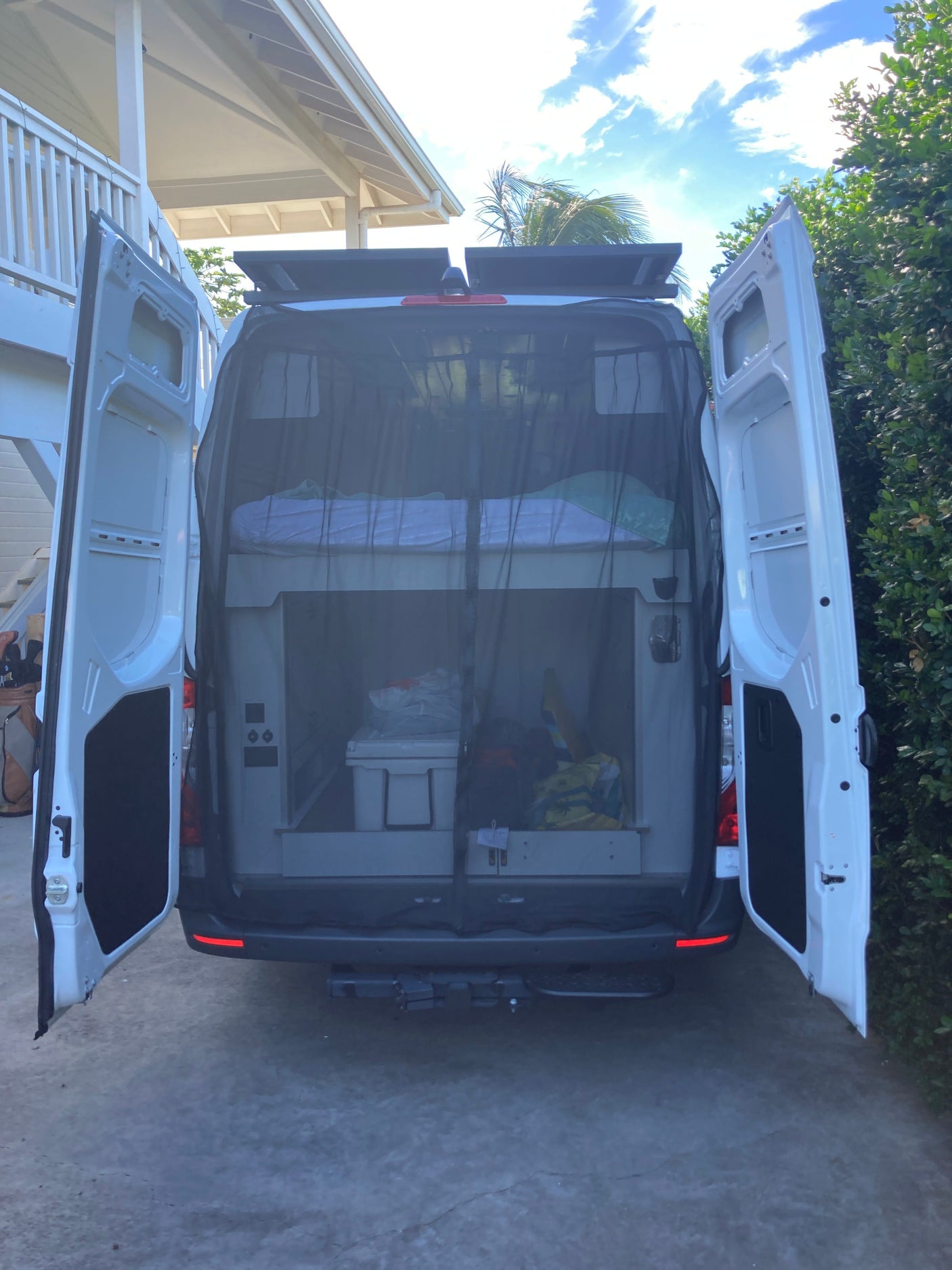 Rear view of an RV rental camper van with open doors, revealing custom bunk beds, mosquito net, and ample storage inside.