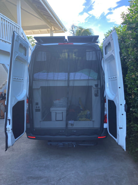 Rear view of an RV rental camper van with open doors, revealing custom bunk beds, mosquito net, and ample storage inside.