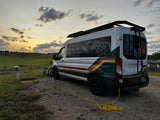 This "VANDOIT" rv rental camper van is parked at a scenic campsite during sunset, hooked up and ready for adventure.