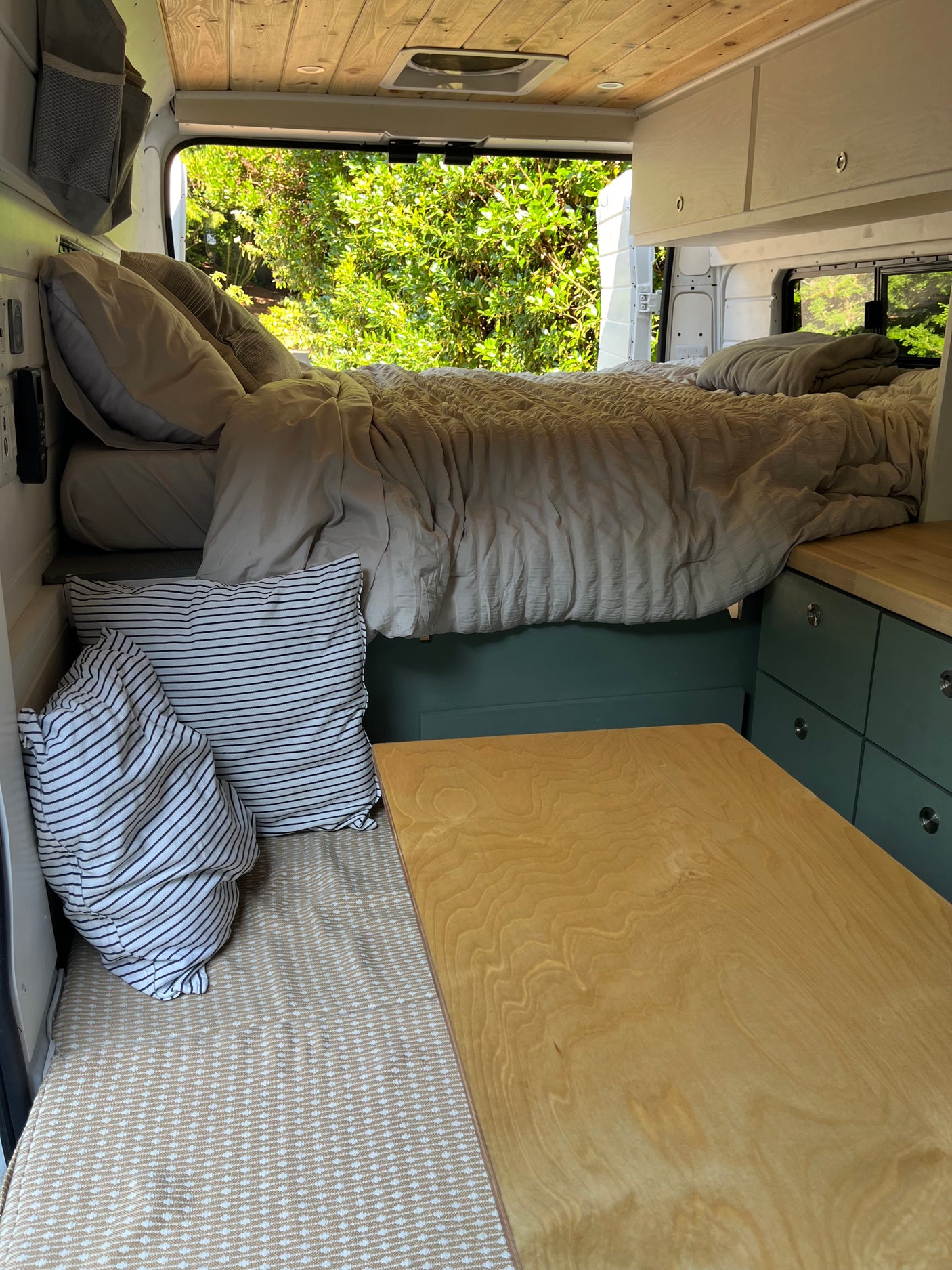 Cozy RV rental interior with bed, wood accents, and lush green views outside.