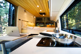 Bright RV rental interior: modern kitchen, cozy bed, laptop desk, and scenic window view. Ideal for van life.