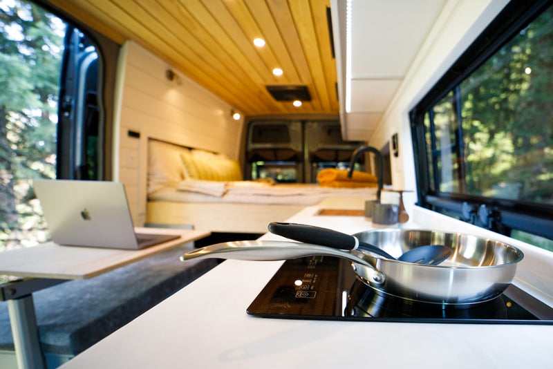  and a pull-out table with mugs outdoors.|This RV rental showcases a modern camper van interior with a cozy bed — photo 16