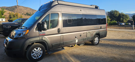 Your next RV rental adventure! This grey Ram ProMaster camper van is parked on a sunny gravel lot, ready for the open road.