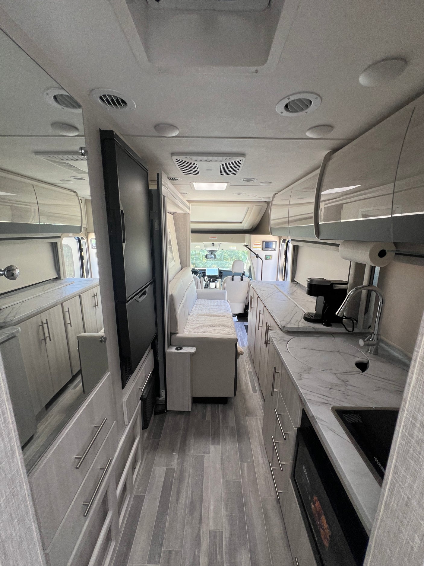 Bright RV rental interior: marbled kitchen, sleek grey cabinets, comfortable living area, and cockpit view for travel.