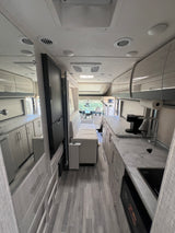 Bright RV rental interior: marbled kitchen, sleek grey cabinets, comfortable living area, and cockpit view for travel.