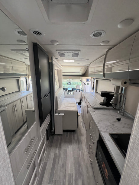 Bright RV rental interior: marbled kitchen, sleek grey cabinets, comfortable living area, and cockpit view for travel.