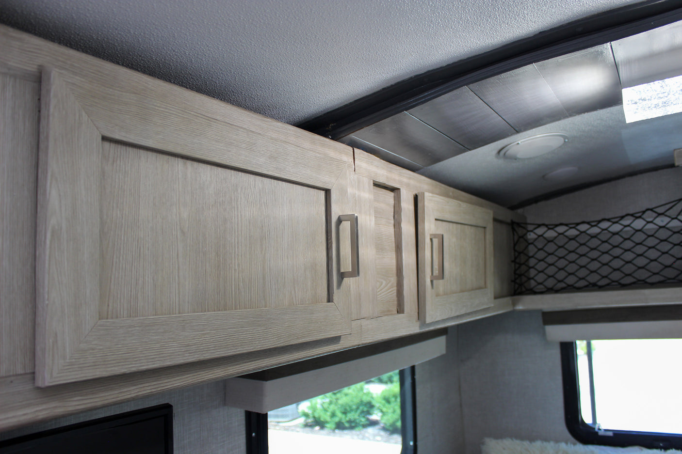 Modern light wood-grain overhead cabinets & storage net in an RV rental, showing clean interior design.