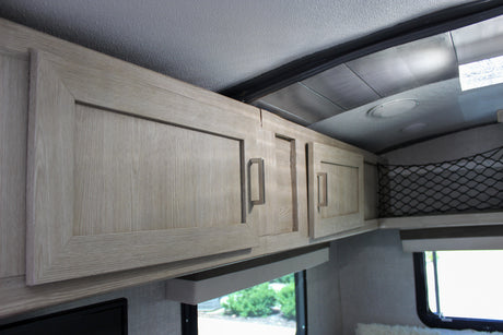Modern light wood-grain overhead cabinets & storage net in an RV rental, showing clean interior design.