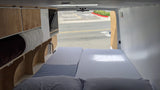 RV rental's custom wood interior: bed, cabinetry, and stored items. Street view from the open rear doors.