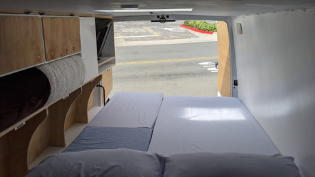 RV rental's custom wood interior: bed, cabinetry, and stored items. Street view from the open rear doors.