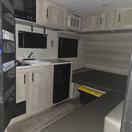 RV rental interior: well-equipped kitchenette with microwave, fridge, AC unit, and adaptable seating/sleeping area.