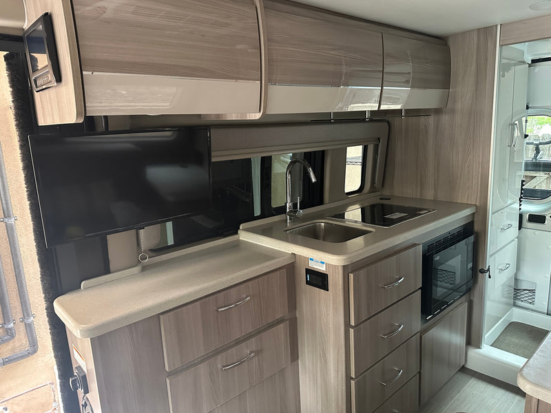 Modern RV rental interior: kitchen with sink, cooktop, microwave, and TV, alongside a shower unit. — photo 3