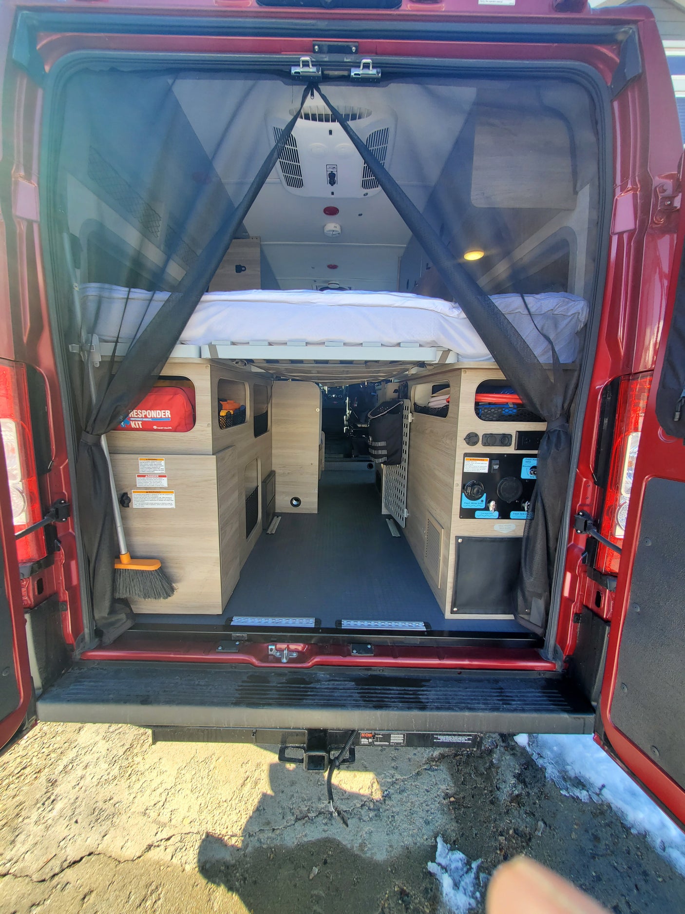 Inside a red camper van for rv rental, showing the bed, storage, utility panel, and mosquito net at the rear.