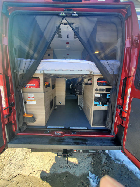 Inside a red camper van for rv rental, showing the bed, storage, utility panel, and mosquito net at the rear.