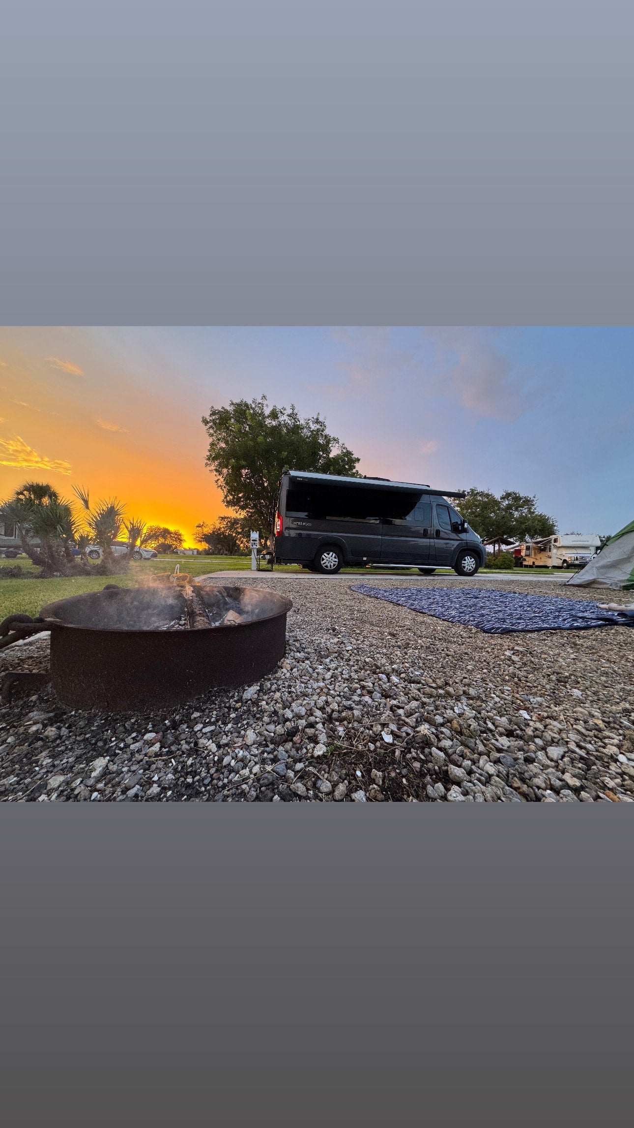 An RV rental parked at a serene campsite with a smoking fire pit and vibrant sunset. — photo 10