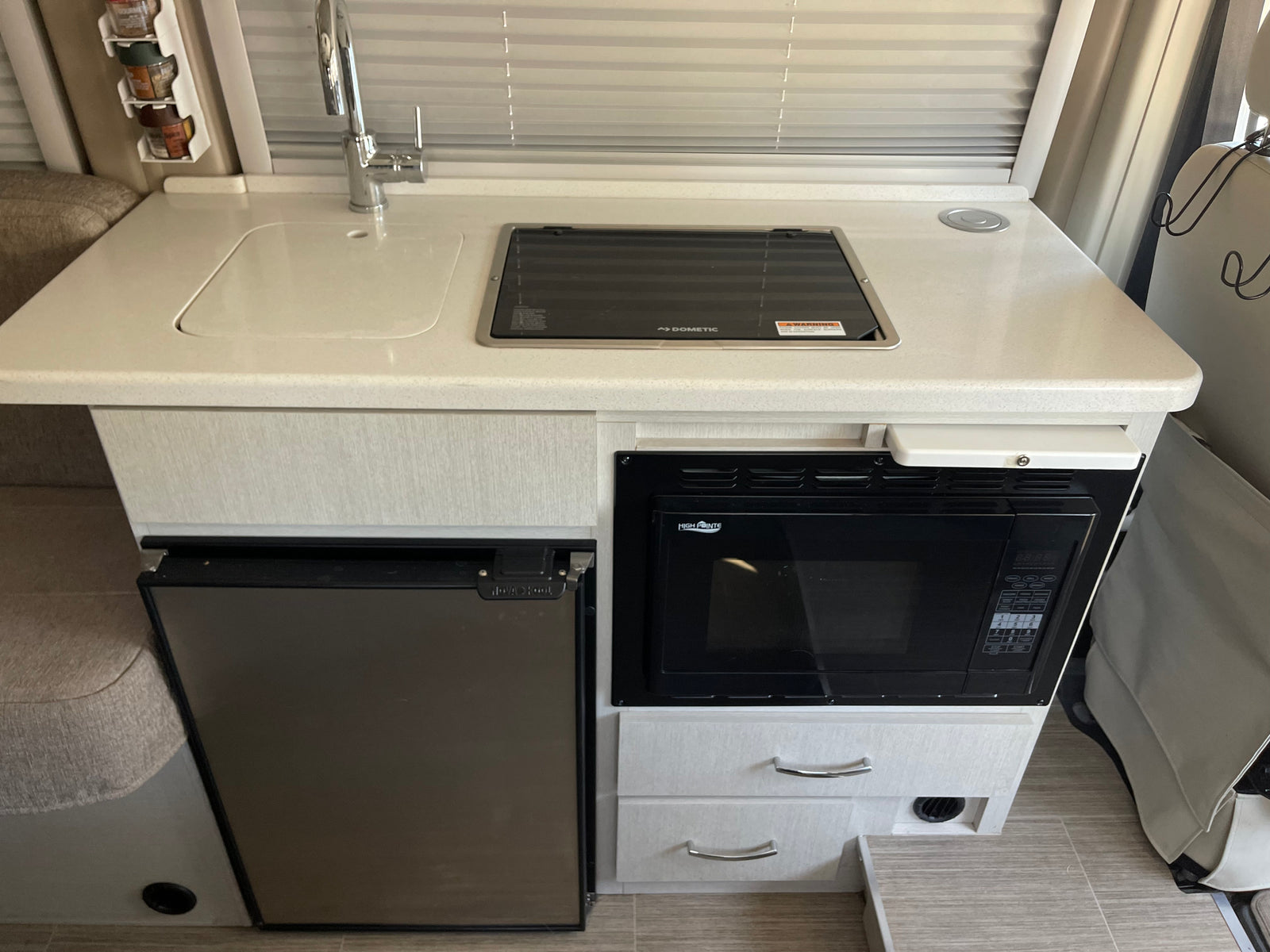 RV rental kitchen with a bright countertop, sink, Dometic cooktop, Nova Kool fridge, and High Pointe microwave, ideal for travel cooking.
