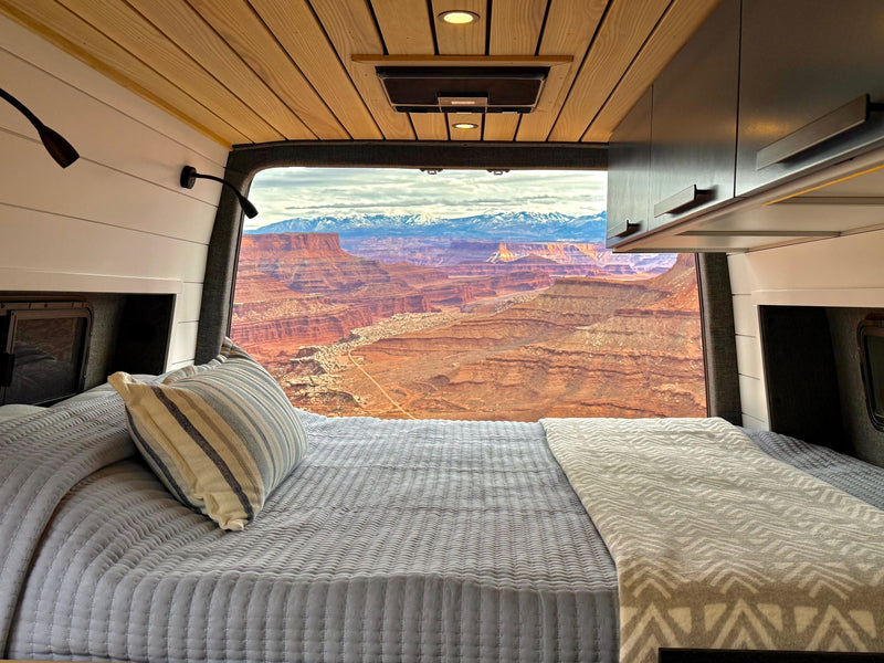 Inside a cozy RV rental, a neatly made bed offers panoramic views of red rock canyons & distant snow-capped mountains. — photo 3