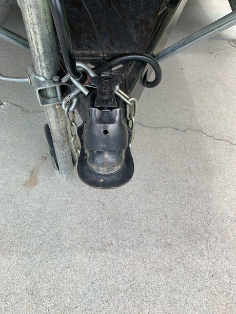 RV rental trailer hitch coupler and safety chains, connected to the A-frame on concrete.
