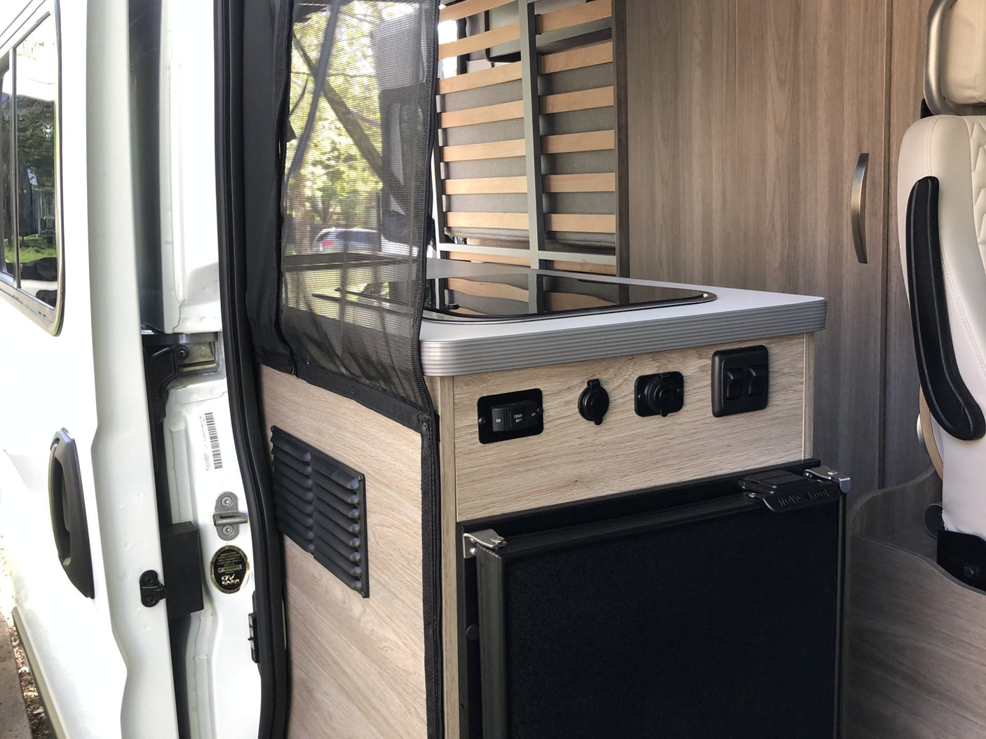 RV rental camper van interior showing kitchenette with stove, fridge, and slatted bed frame. Ready for adventure.