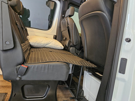 Inside an RV rental, black seats fold down to a flat bed. A cream pillow rests on the padded surface for travel comfort.