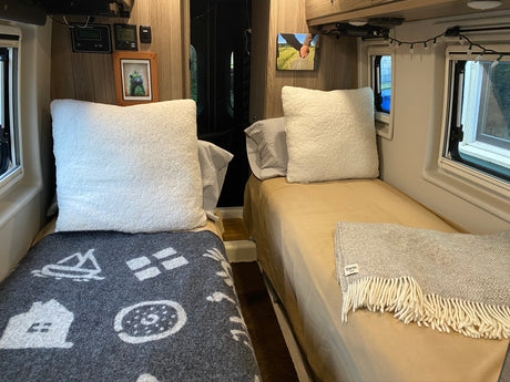 Inside a cozy RV rental: two twin beds with plush pillows, blankets, and personalized decor details.
